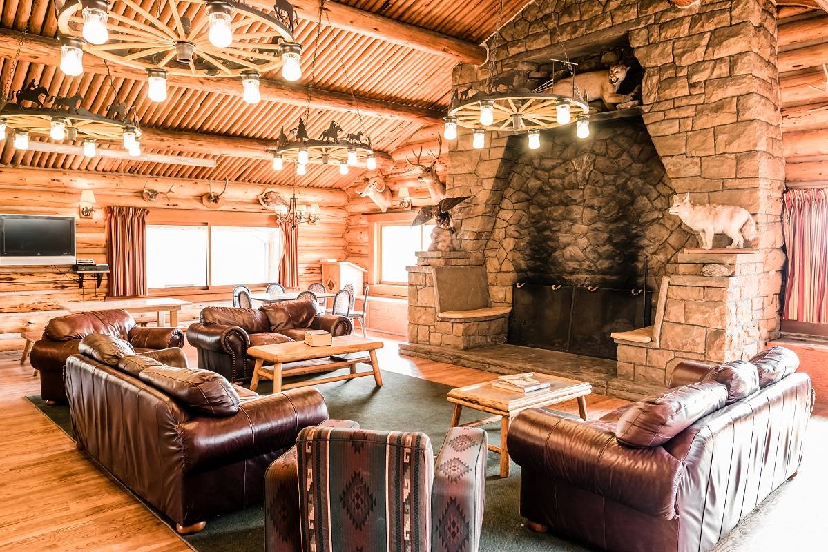 gallery-lodging-new-img1-lodging-near-yellowstone-updated (1) A cozy log cabin living room featuring a warm fireplace, wooden beams, and rustic furnishings, inviting relaxation and comfort.